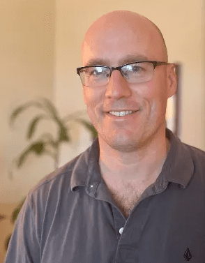 A man with glasses and bald head smiling.
